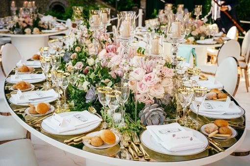 Gold distressed mirrored oval table set for dinner with gold cutlery and opulent floral centrepiece