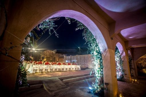 High end destination wedding with large floral arches and long banqueting tables set for dinner with stunning red rose flower arrangements
