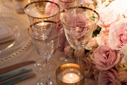 Gold rimmed glasses, gold etched candles and silver cutlery on a long banqueting table with pink rose floral centrepiece at Blenheim Palace lavish wedding