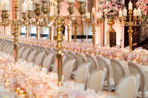 Opulent tablescape for a luxury wedding with long tables, full floral runner, gold candelabras, lavish flower arrangements on top of gold urn and plinth inside the Long Library at Blenheim Palace