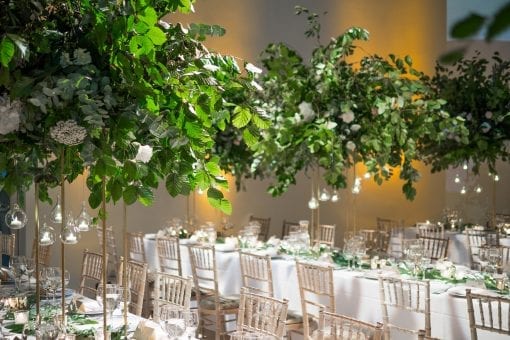 Gorgeous floral and leafy table centrepiece with delicate candles in glass baubles at a luxury celebrity wedding reception in London