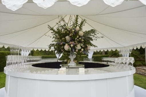 Beautiful white gloss bar under a Raj tent with pretty white draping and stunning floral centrepiece at a luxury wedding