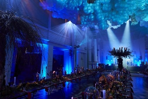 Two long dinner tables underneath a ceiling of white cloud balloons at a party in London
