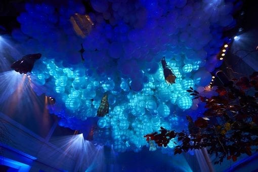 White balloons hanging from a ceiling with decorative dresses hanging underneath for a surrealist party in London