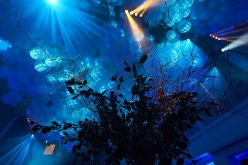 White balloons and decorative tree inside a room lit with blue lighting for a Surreal themed birthday party