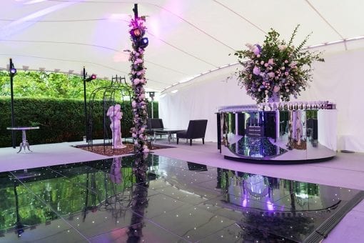 Black gloss dance floor with pin spots, purple lighting design and mirror round bar for an wedding afterparty under a white stretch tent for a high end wedding