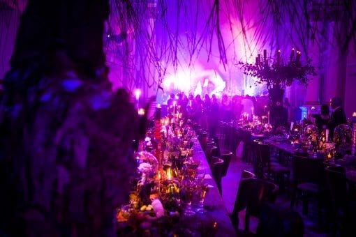 A private birthday party inside One Marylebone, with a surrealist theme, with long tables, aerial floral designs and candles