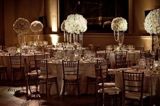 Round dining tables with large rose floral arrangements and pearls for a Royal Nigerian white wedding