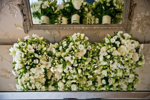Three white floral wedding bouquets balanced on a mirrored table at a luxury wedding reception