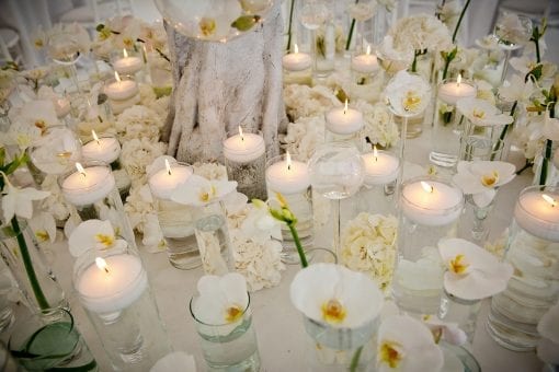 White orchids and hydrangeas with candles arranged on a white cloth table at a luxurious wedding