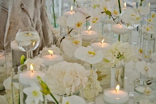 White orchids, hydrangeas and candles arranged on a white cloth table at a high end wedding
