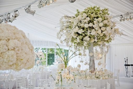 Decorative floral tree centrepieces with large white hydrangea arrangements in white marquee for a luxury wedding reception