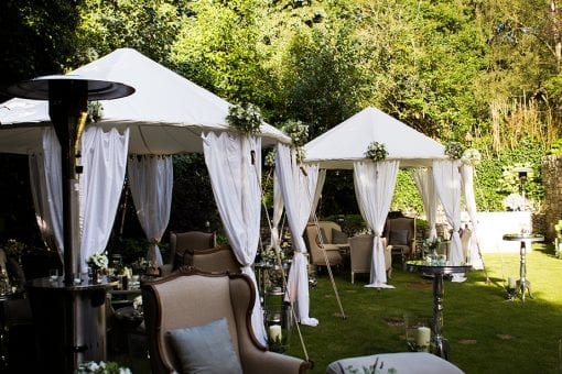 Raj tents with white draping and lining set with luxurious soft seating and mirror topped tables in a garden on a private estate