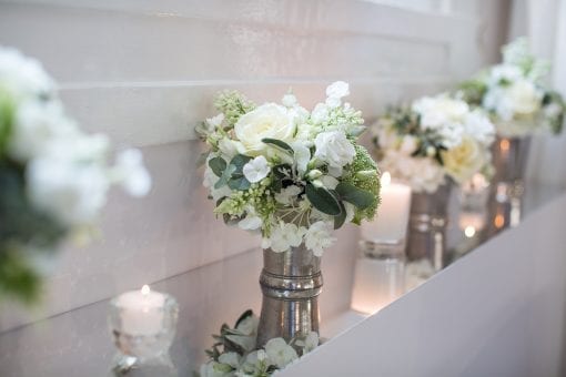 Silver greenery and white florals in silver vessels surrounded by tea lights at a private event