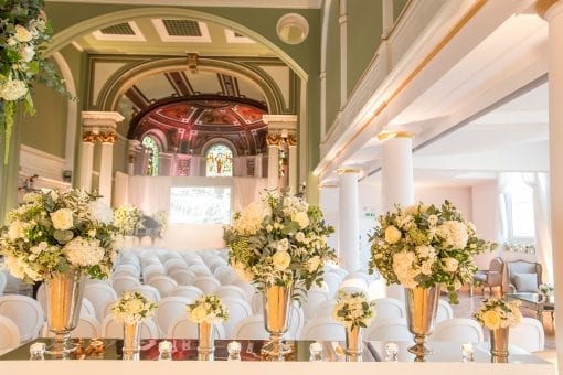 Elegant green and white florals with a ceremony set up with white chandelle chairs inside One Marylebone