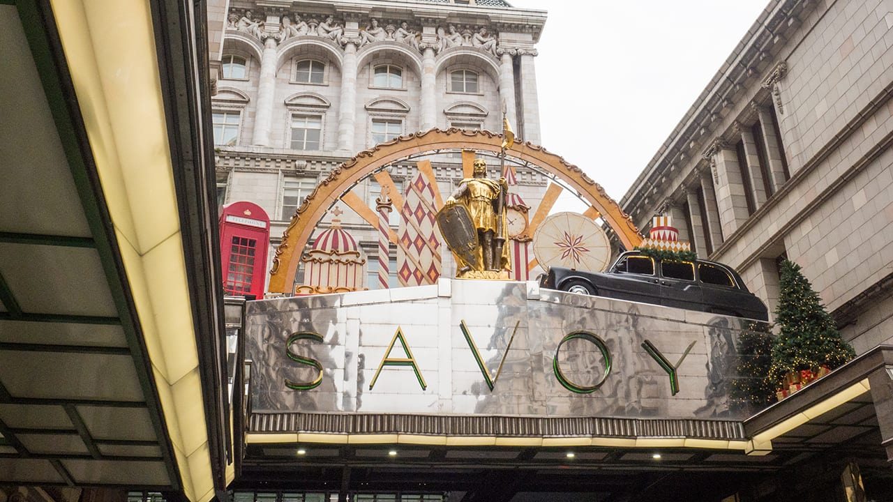 The exterior of the Savoy Hotel in London with gold knight statue and taxi cab decoration