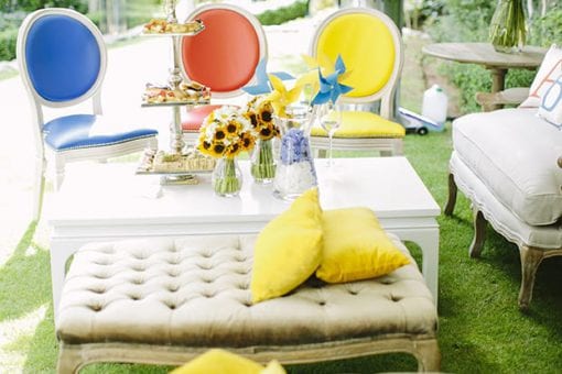 Sunflowers in glass vases on tables outside with seating area under white raj tents for a luxury kids party