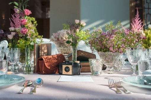 Vintage cameras, vintage books positioned for a vintage styled table setting with vintage glassware and pretty flowers.