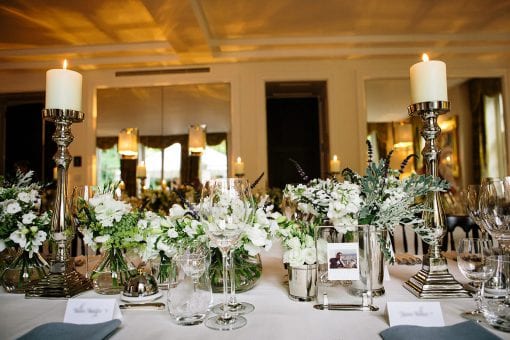 Elegant table setting for dinner on long tables in a private residence in Hamstead, London with pretty white flowers and pillar candles