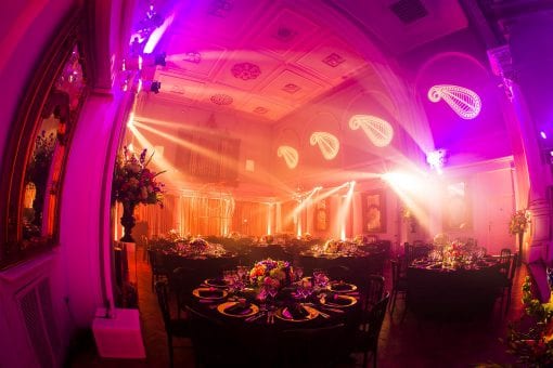 A lavish party set for dinner with round tables and bespoke Indian inspired gobo lighting