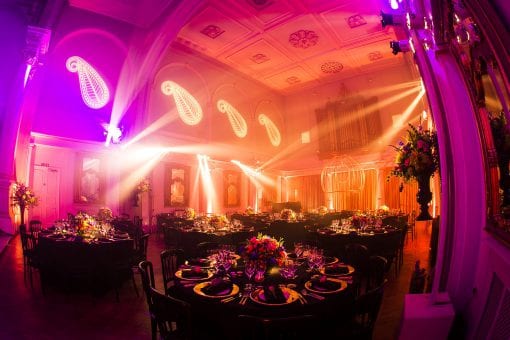 Orange and pink lighting design with bespoke gobo lighting over round tables with Indian inspired flowers at One Marylebone