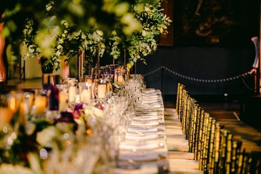 Long banqueting table set for dinner styled with over the top trees and purple flowers at Hampton Court Palace