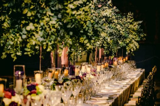 Long tables covered in bright purple flowers and green trees at the Great Hall at Hampton Court Palace for a private birthday party