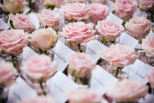 Individual escort cards arranged on a mirrored table with individual pink roses for a luxurious wedding at Villa Pizzo in Lake Como