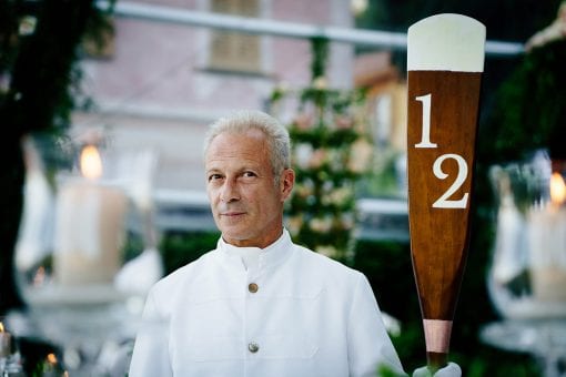 Luxury destination wedding with waiters holding bespoke table numbers on wooden oars at Villa Pizzo in Lake Como, Italy