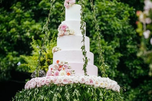 Exquisite five tier white wedding cake decorated with stunning flowers suspended from a glass structure at Villa Pizzo
