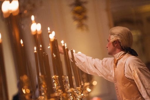 Waiter styled in period costume for a themed bespoke party lighting individual gold candles at the Mandarin Oriental Ballroom in London