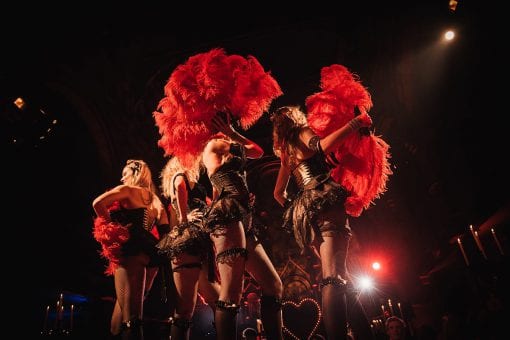 The IT girls dressed in black corsets holding red feather boas at a Moulin Rouge party in Mayfair