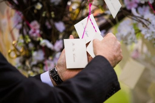 Wedding guest looking through escort cards suspended from pink and white cherry tree at luxury wedding in London Regents Park